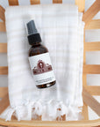 An amber glass bottle laying on top of a natural linen towel above a slatted wood bowl or tray.