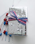 a wrapped box in silver foil stars with red and blue decorative stars next to it