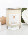 A clear glass candle with natural ivory wax.  On the left is a burlap ribbon and on the right is a magnolia blossom.