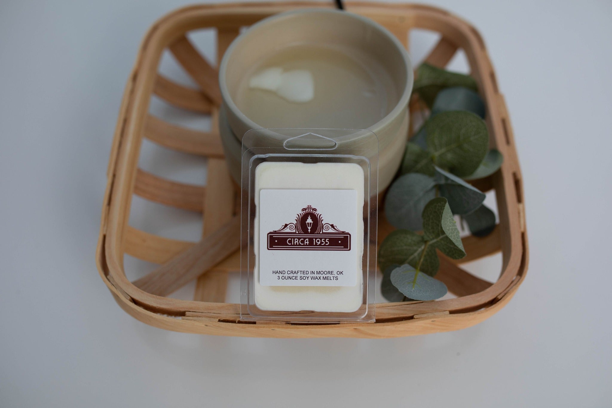 A plastic, six-cavity clamshell melt in a wood basket with a wax melter and eucalyptus sprigs.