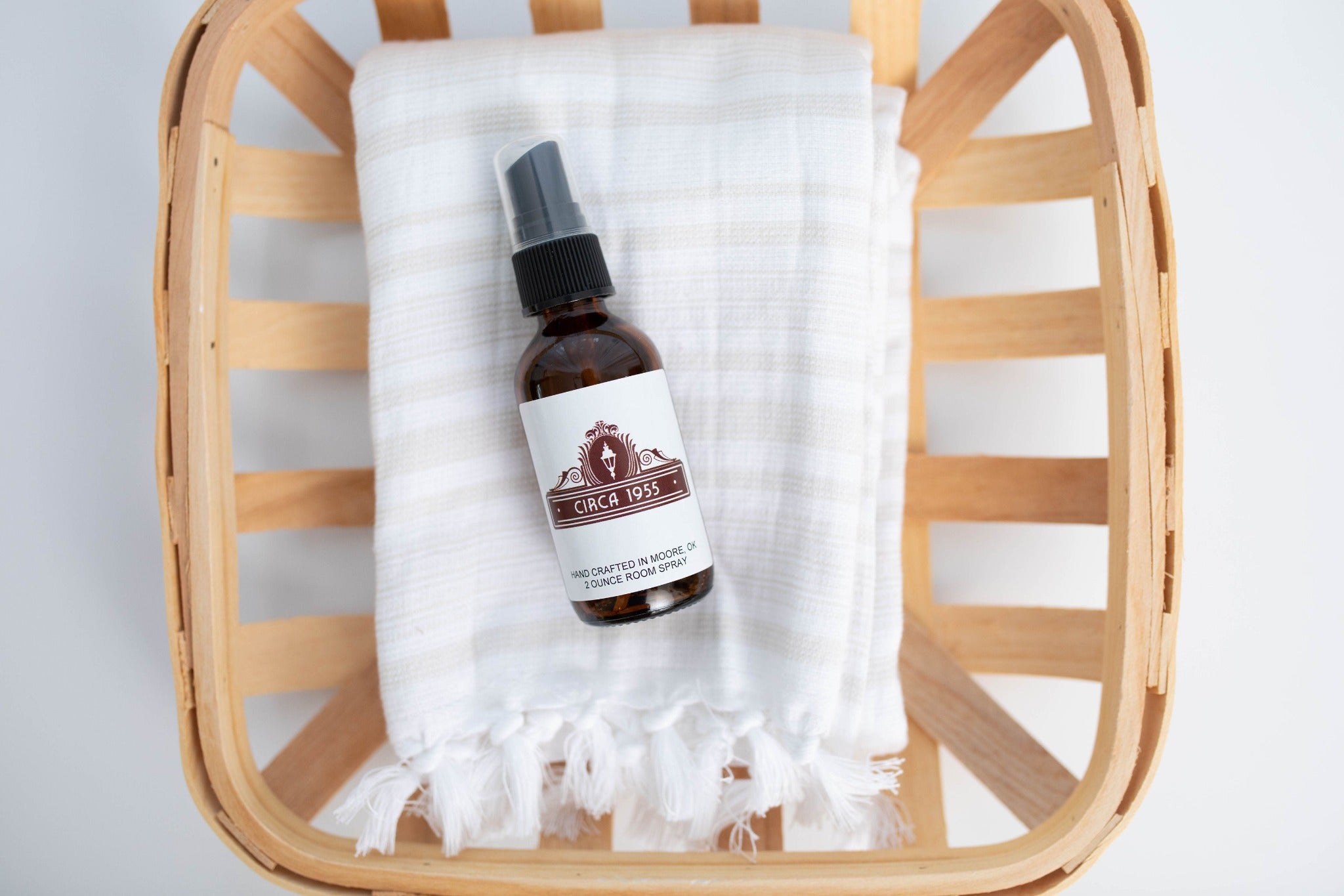 An amber glass bottle laying on top of a natural linen towel above a slatted wood bowl or tray.