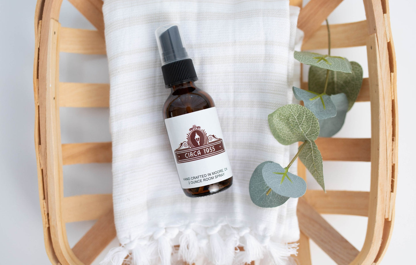 An amber glass bottle laying on top of a natural linen towel above a slatted wood bowl or tray.