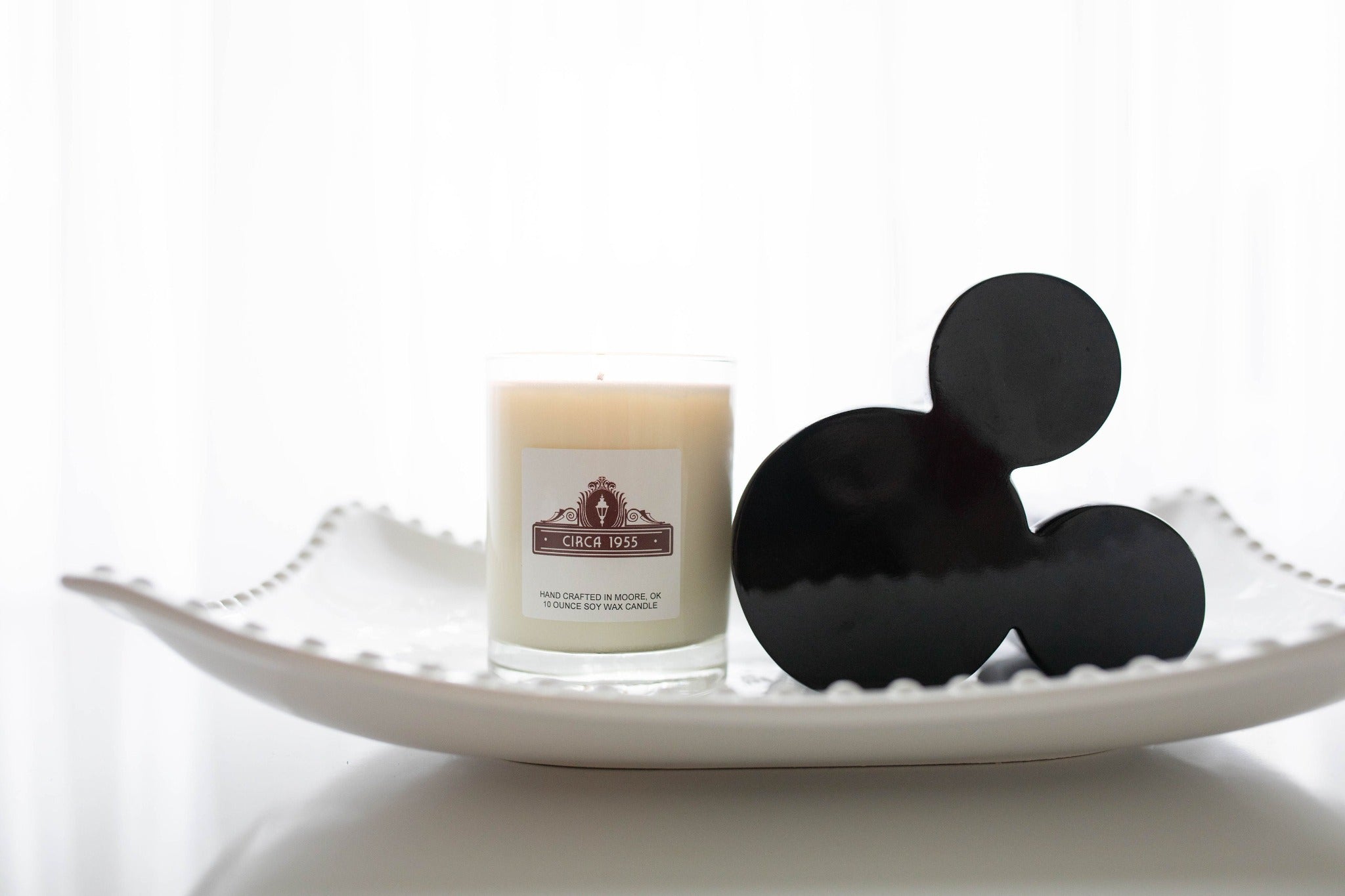 A single wick glass candle on a white hobnail tray with a mickey head on the right.