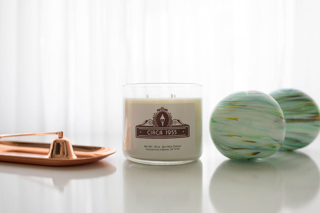 A three-wick clear glass candle with natural ivory wax.  To the left is a copper candle snuffer and to the right is a turquoise, blue and gold swirled decorative orb.