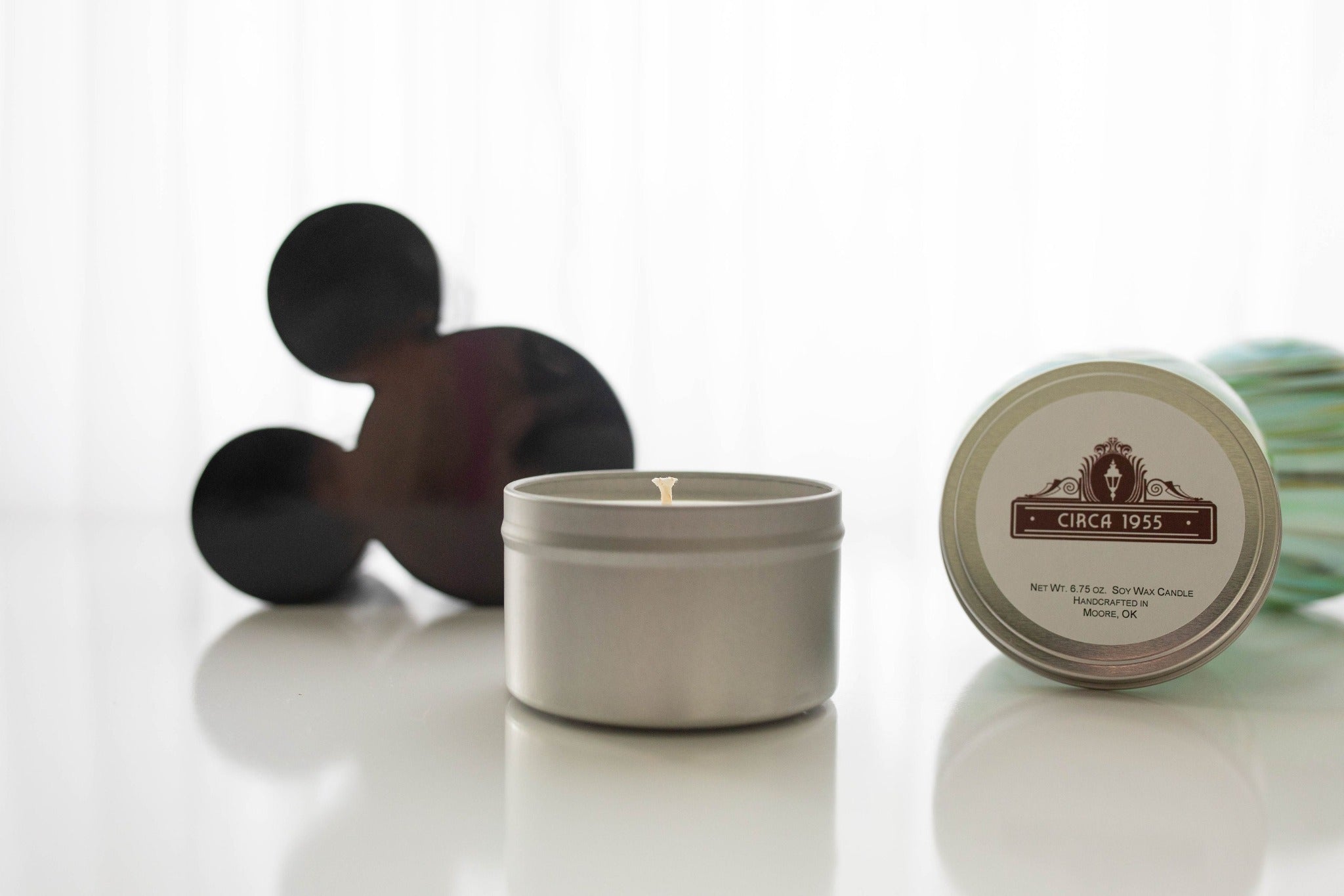 A silver metal candle tin with a small black mickey head behind it