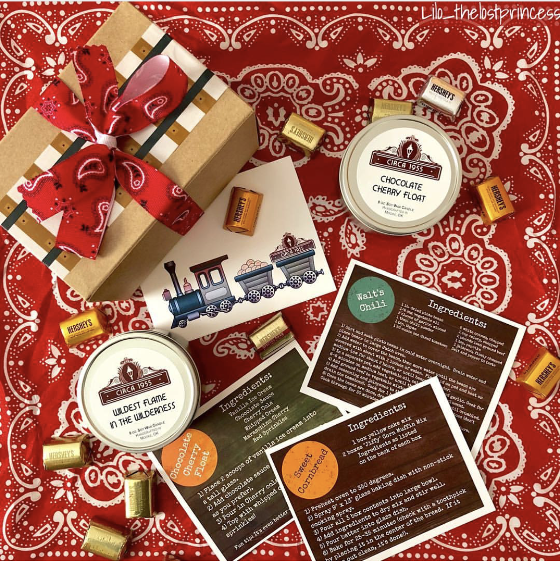 two candle tins on a red bandana with nugget candies, recipe cards and train-track wrapped box