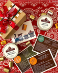two candle tins on a red bandana with nugget candies, recipe cards and train-track wrapped box