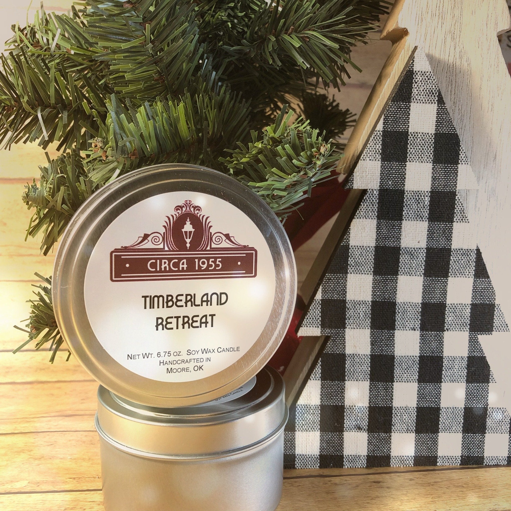 a silver candle tin with a sprig of bpine behind it and a white buffalo plaid tree next to it
