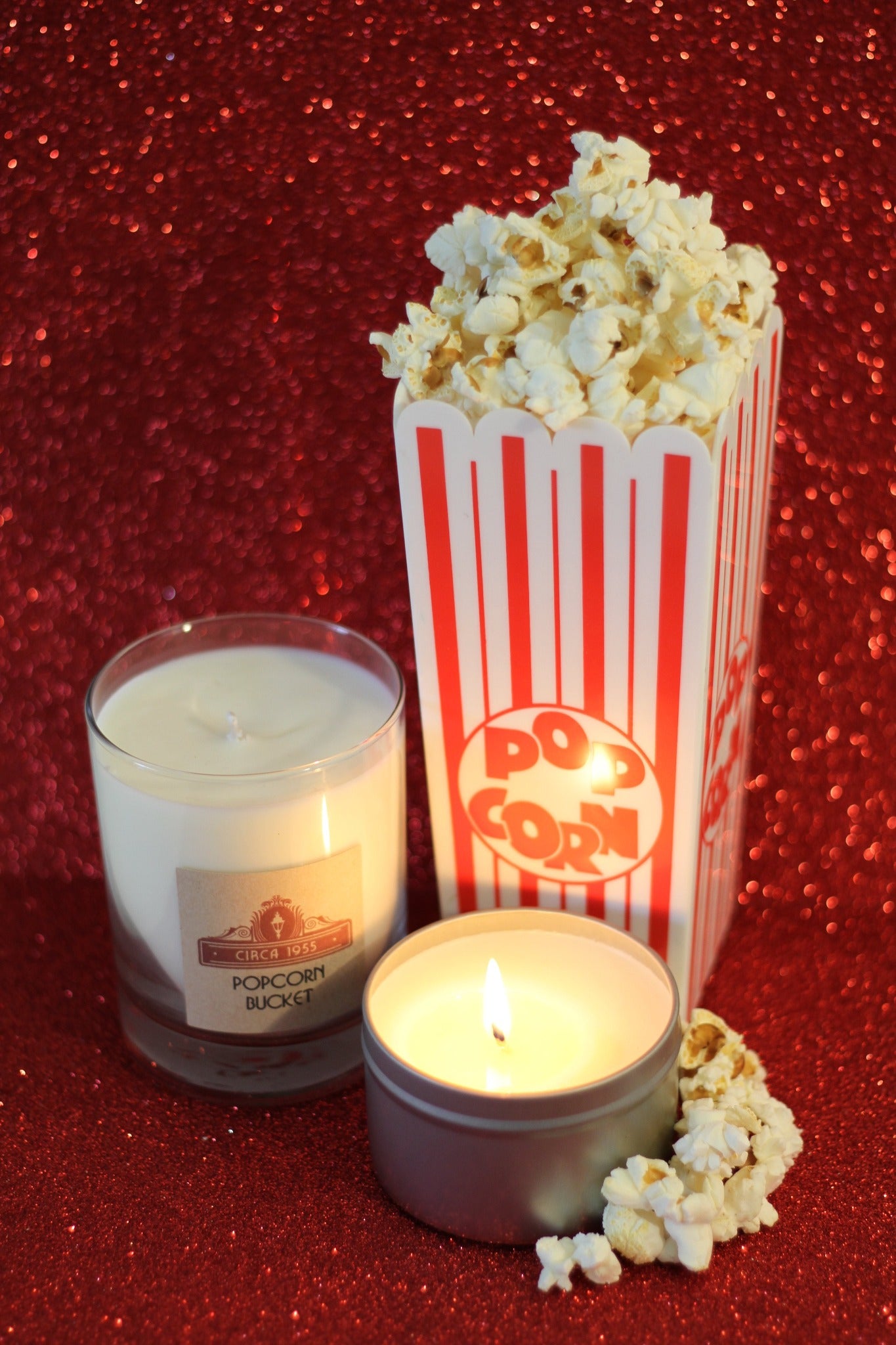a clear glass tumbler candle and a silver candle tin with a container of popcorn