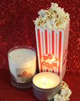 a clear glass tumbler candle and a silver candle tin with a container of popcorn
