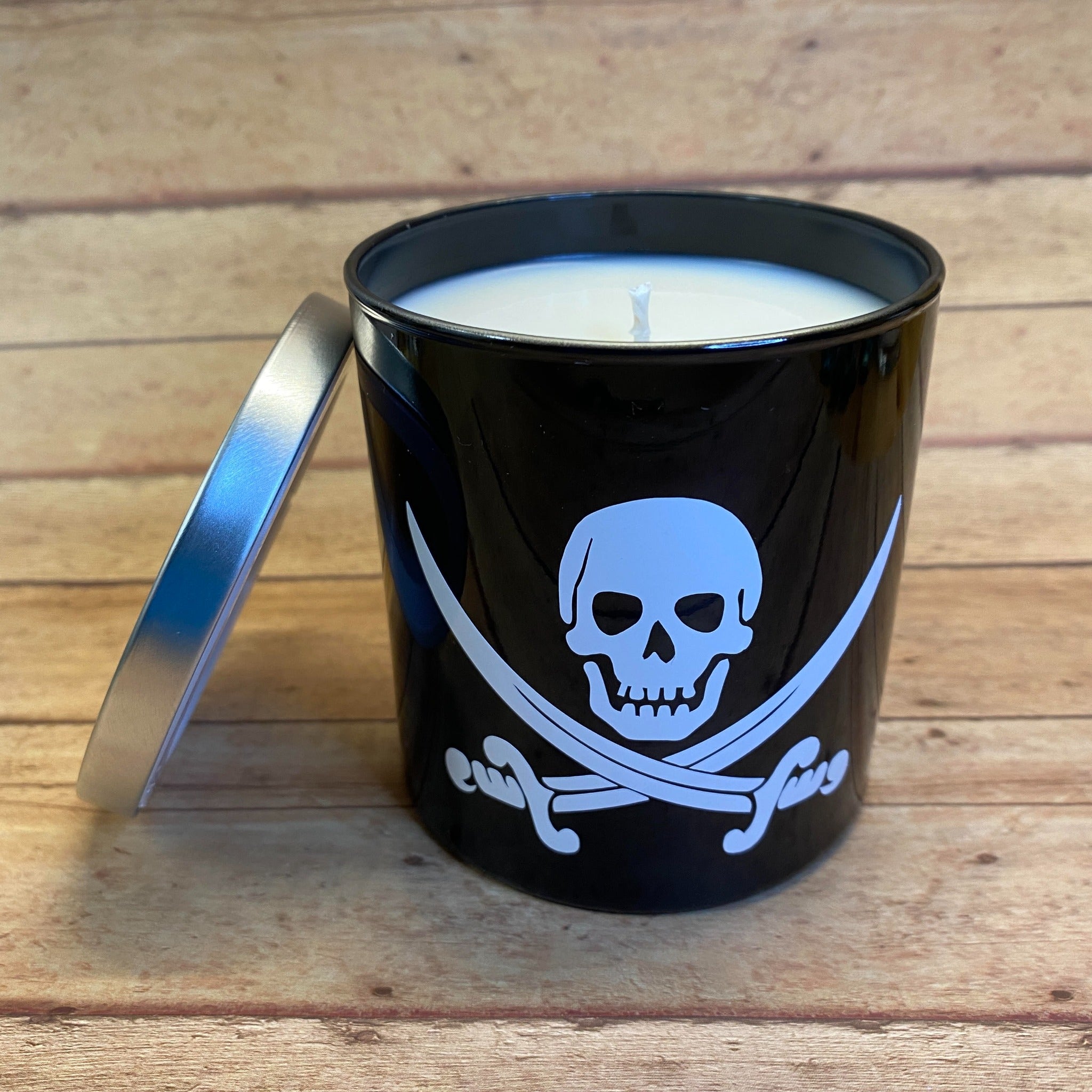 a black glass tumbler candle with the white jolly roger skull and crossed swords on it
